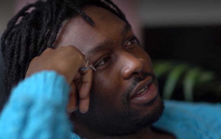 A portrait of a black masculine-presenting person with beard and hair threads