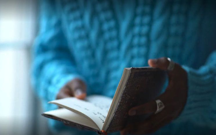 A person in a blue top and rings on fingers browsing through the pages of a small book