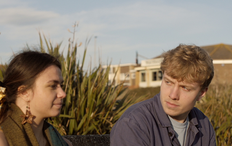A young woman and man sit on a bench, the man is looking at the woman.