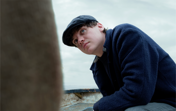 A man in a cap bending down and looking at the camera.