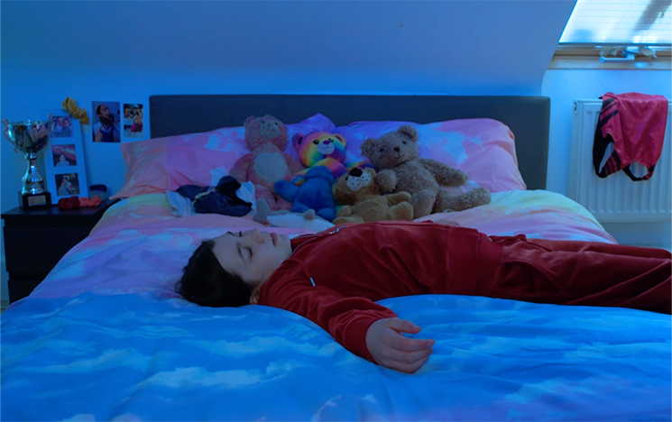 A girl in a red tracksuit lying on a bed in blue lighting.