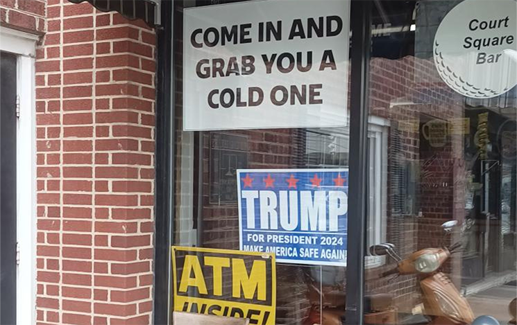 A cafe window with signs about Trump and coming inside to get a drink