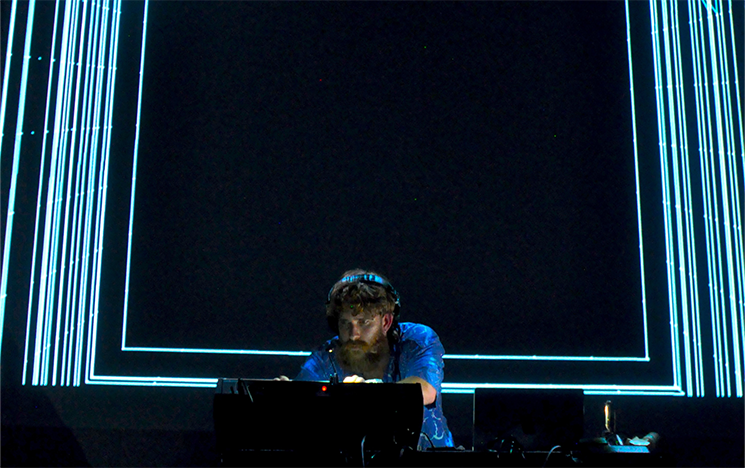A man leaning over a DJ deck backlit by blue lighting.