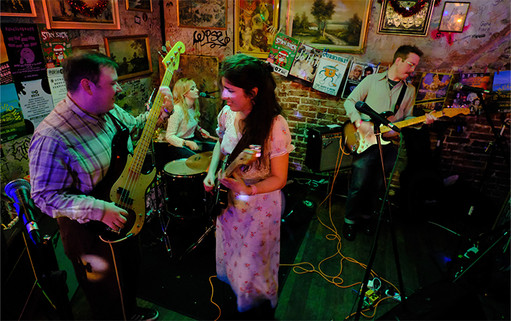 A man and woman playing a guitar and singing in a band