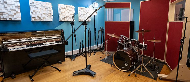 Music Studio 1 Live Room, including upright piano, drum kit, mic stands and acoustic treatment