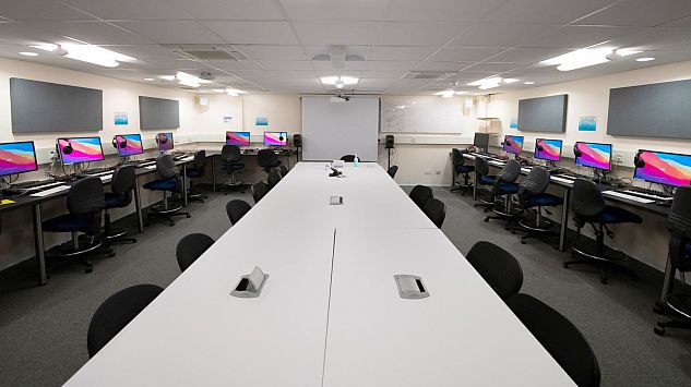 A computer lab full of Apple Mac computers, with desks and chairs.