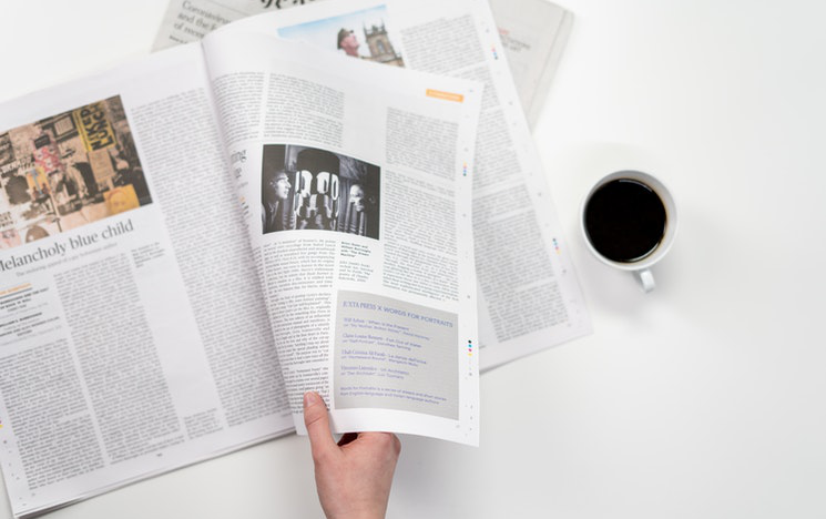 Image of a newspaper with a hand and a black coffee.