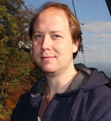 Portrait image of Dr Warrick Roseboom in front of a slope with trees and lightly clouded sky.