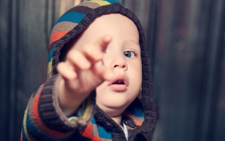 Toddler in a colourful hoody points at the camera