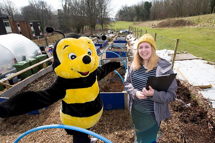 Dr Beth Nicholls is standing in an allotment with someone in a bee costume