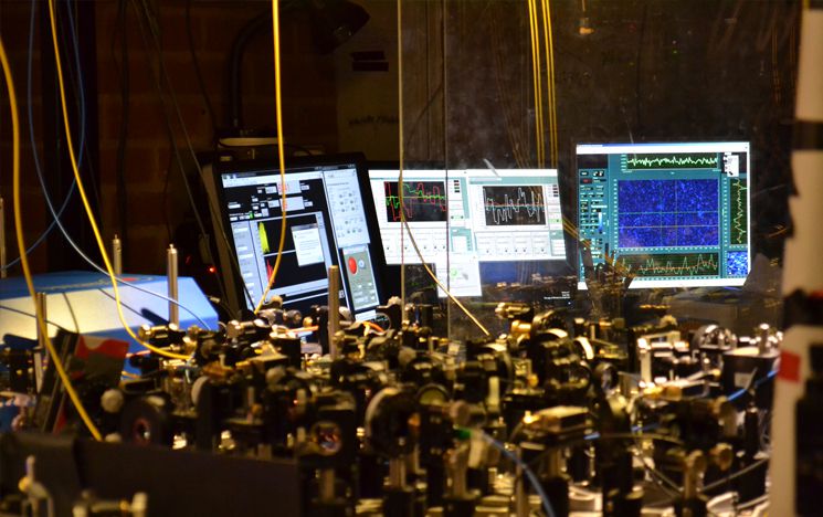 Computer screens with scientific data on them and optics in the foreground