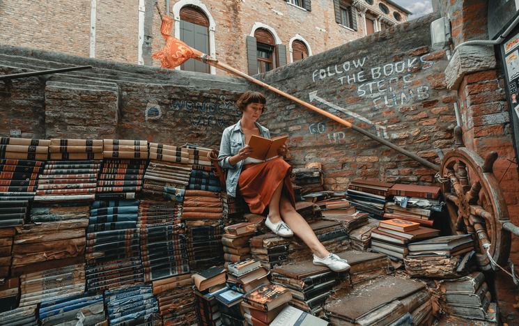 Women sits reading on piles of books