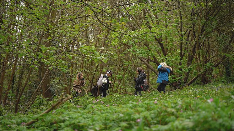A group of children in a woodland with headphones on looking for birds