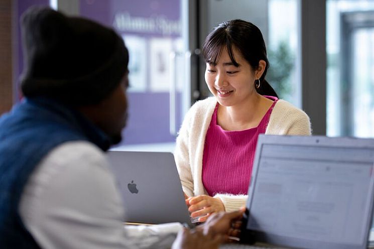 Two students sat at a desk using laptops