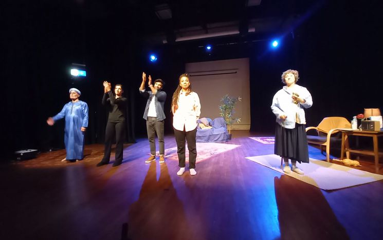 Five cast members stand in the light applauding the audience