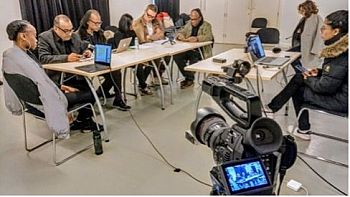 A camera films acrtors reading around a table while researchers liaise with participants at a computer