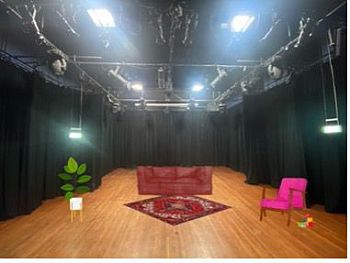 A simple stage design of a carpet, sofa, chair and pot plant on a stage