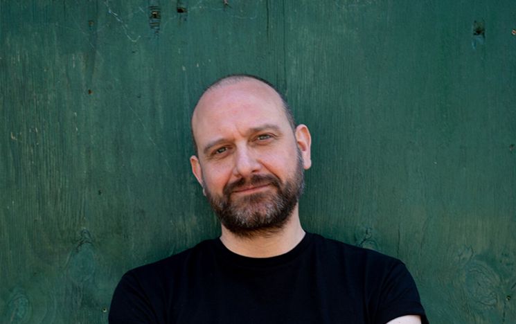 Keir Milburn (white man with beard wearing black t-shirt against a green background)