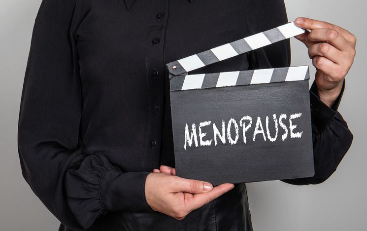 Showing torso of woman holding a clapper board with 'menopause' written on it