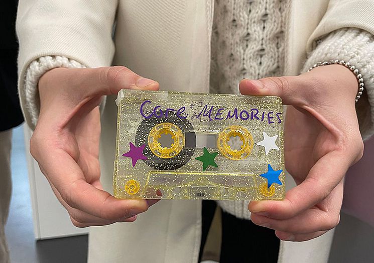 A photo of a person holding a cassette tape covered in glitter and stars, with hand written "core memories"