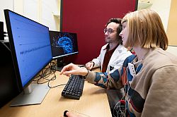 Researcher and participant looking at two computer screens, one showing participants heart beat and other physiological measures