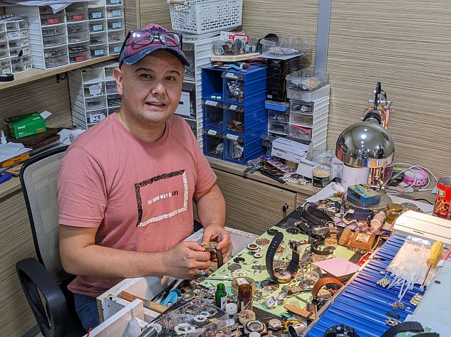 Abdullah (wearing a pink top and baseball cap) sat in the watch shop where he works
