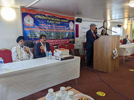 Delegates of the Afghan Hindus and Sikhs 2022 National Conference sat at table while another man stands at a podium talking