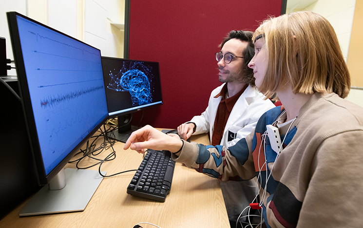 Two people studying a brain image and stats on two computer screens.