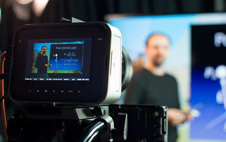 A camera points at a man demonstrating a presentation.