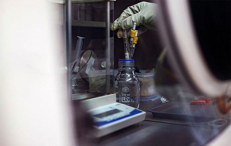 A gloved hand holding a piece of apparatus in a jar for a chemistry experiment