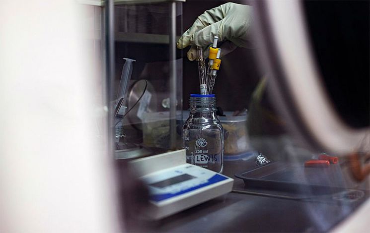 A gloved hand holding a piece of apparatus in a jar for a chemistry experiment