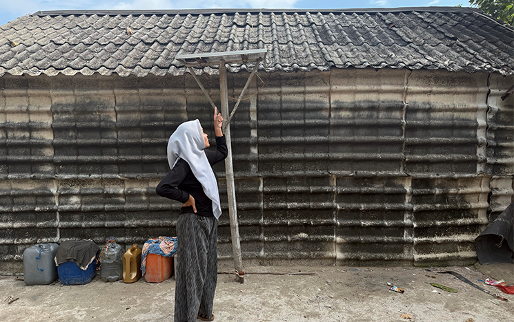 POWERE team member standing outside a wooden hut tracking solar panel arrangements.