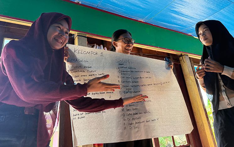 Women presenting to a class while holding a paper with writing on