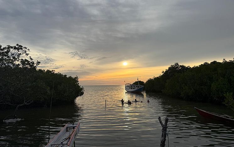 Sunset over the sea with swimmers and boat