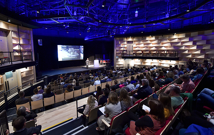 Students sitting in rows of seats watching a performance on stage at the Attenborough Centre