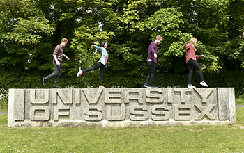Students standing on the University of Sussex entrance sign
