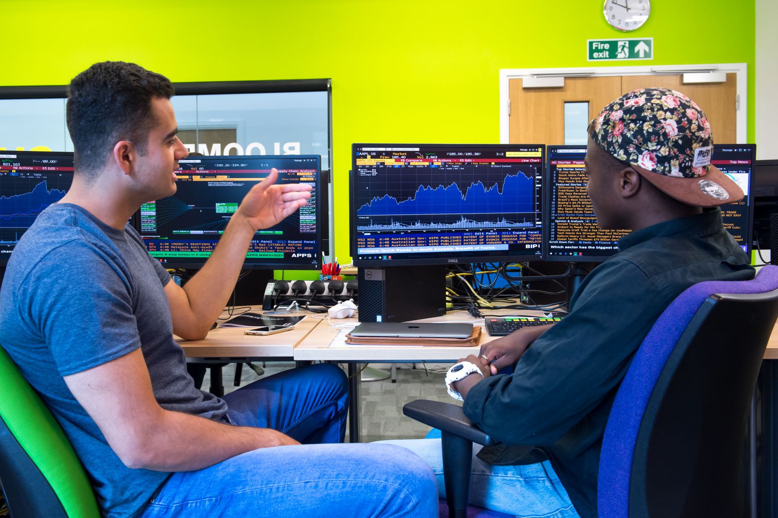 Two students in the Bloomberg Financial Markets Laboratory, in front of terminal screens display trading graphs and news items