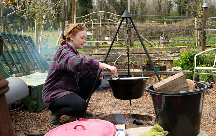 Woman cooking something over a fire in a garden