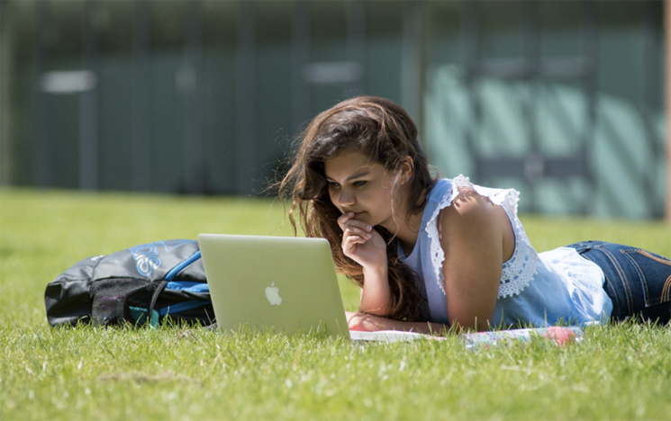 Student sitting outside on the grass using a computer