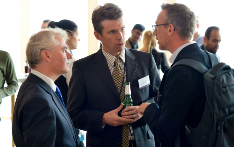 Icon: Three professors standing up in a discussion at a conference