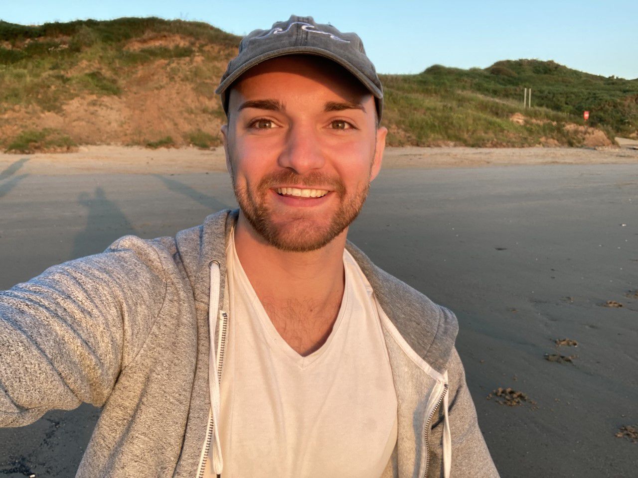 Photo of James on a walk, smiling at the camera in a cap