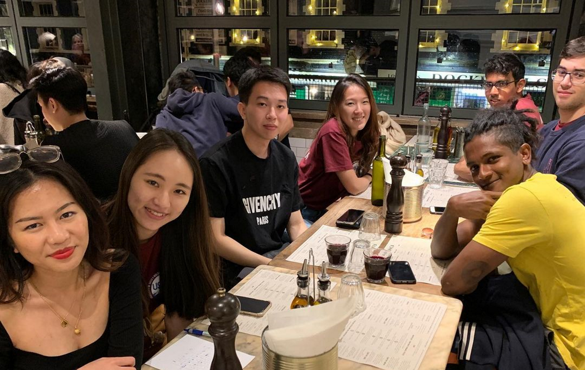 Several students at a restaurant table at night smiling