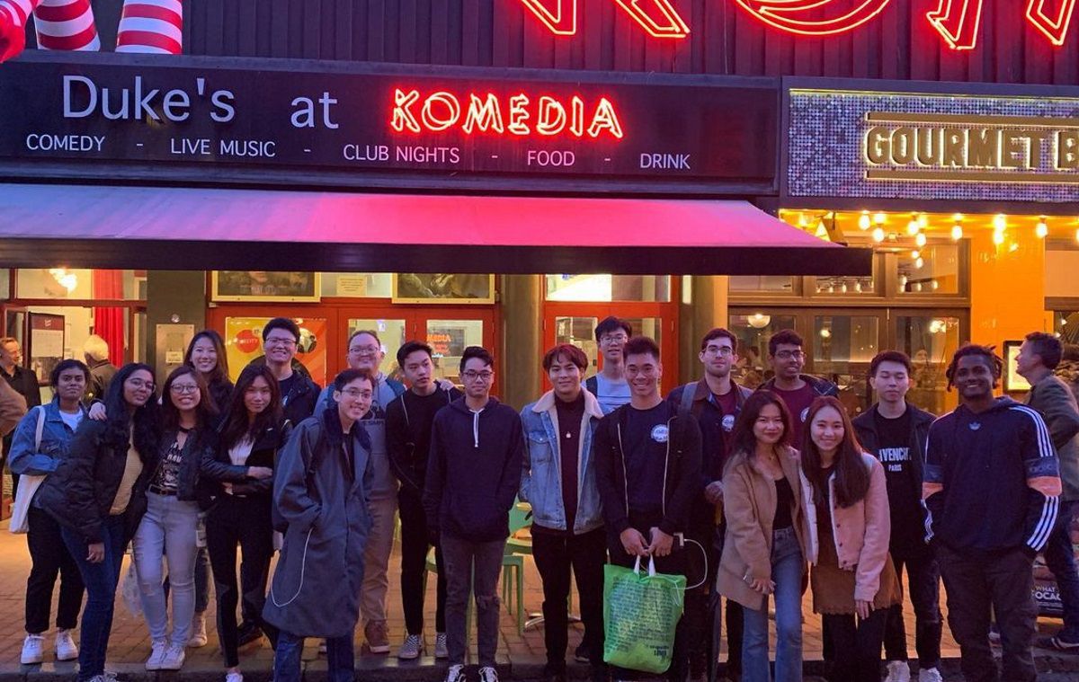 A large group of students pose for a photo in a dimly lit street in Brighton at dusk