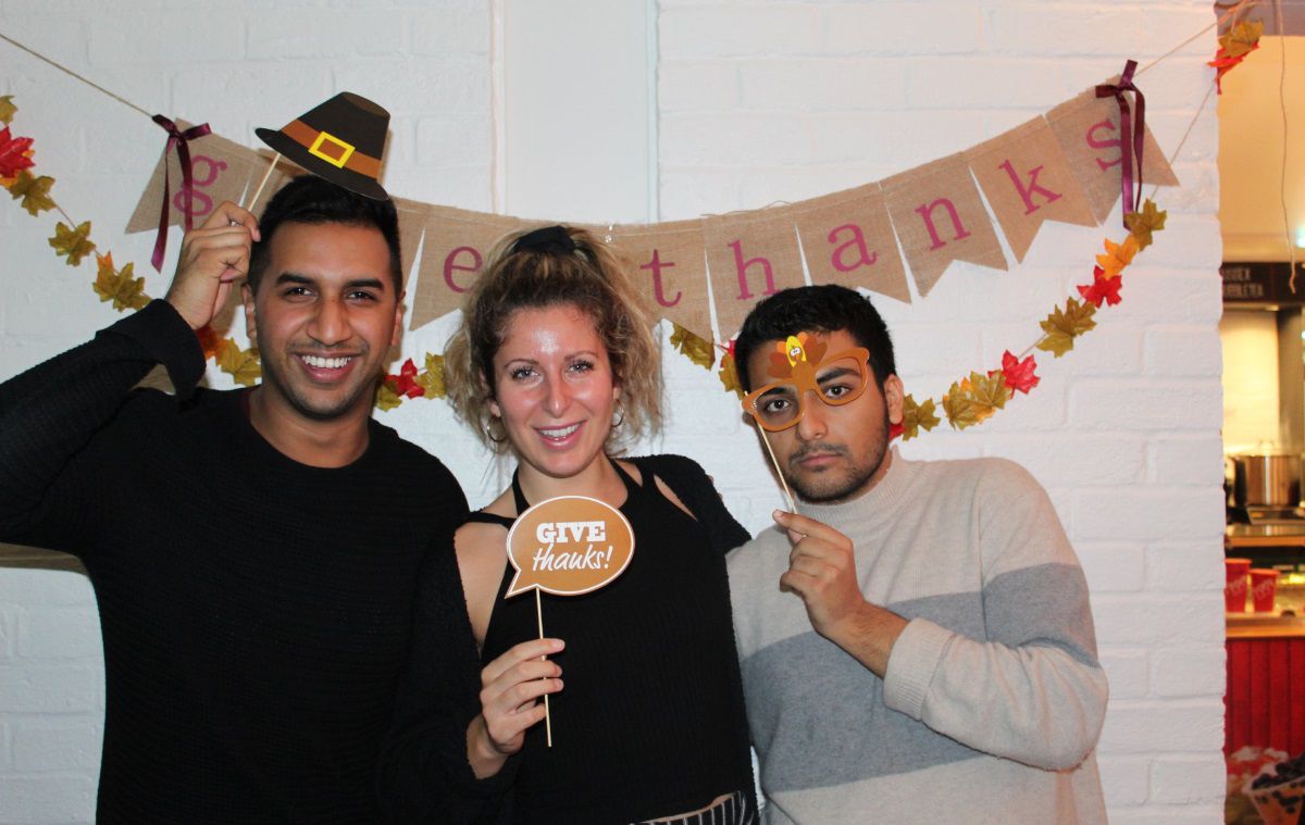 Three students with props saying ’Give thanks’ smil to camera