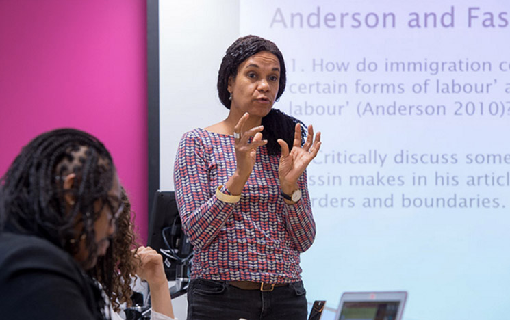 Lecturer infront of a smartboard teaching to a class about anthropology