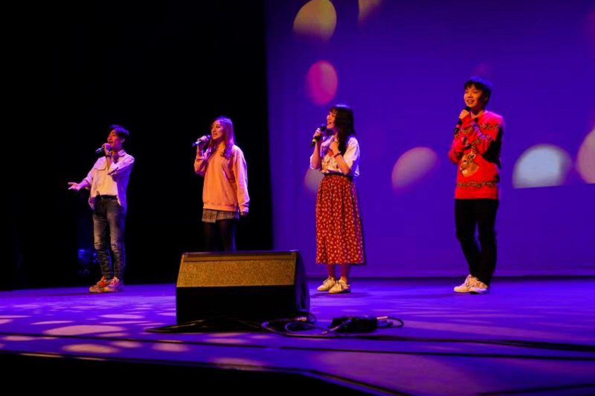 Four students singing on a stage, smiling and looking into the audience