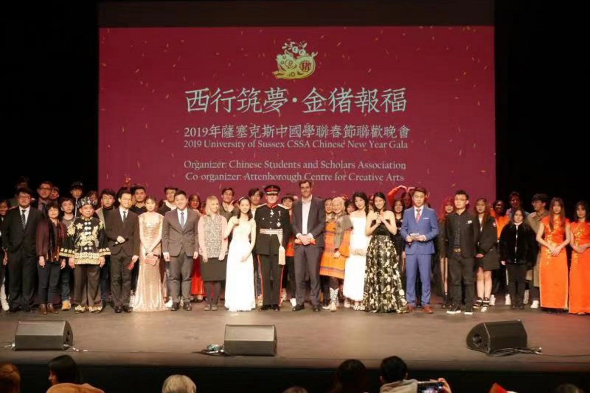 Performers stand on a stage while a crowd applauds