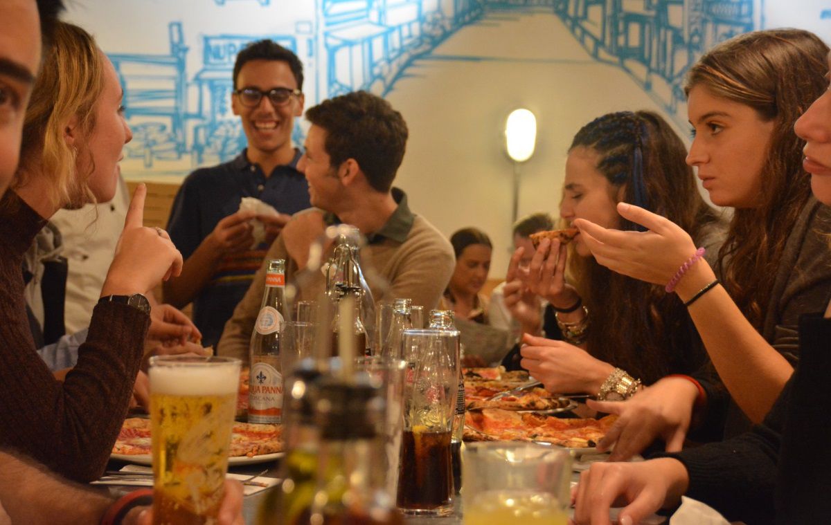 Several students eat pizza in a restaurant chatting to each other