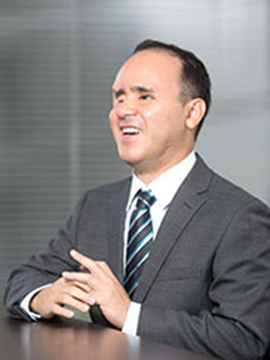 A man in a business sits behind a desk smiling