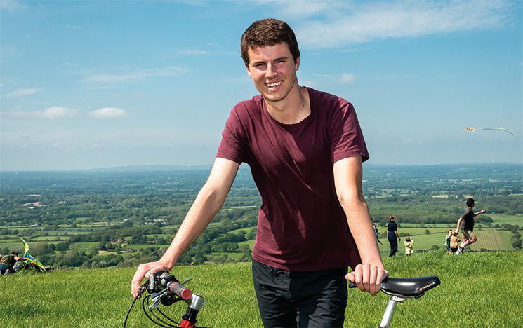 Tom standing with his bike, with the fields of the Sussex South Downs in the background